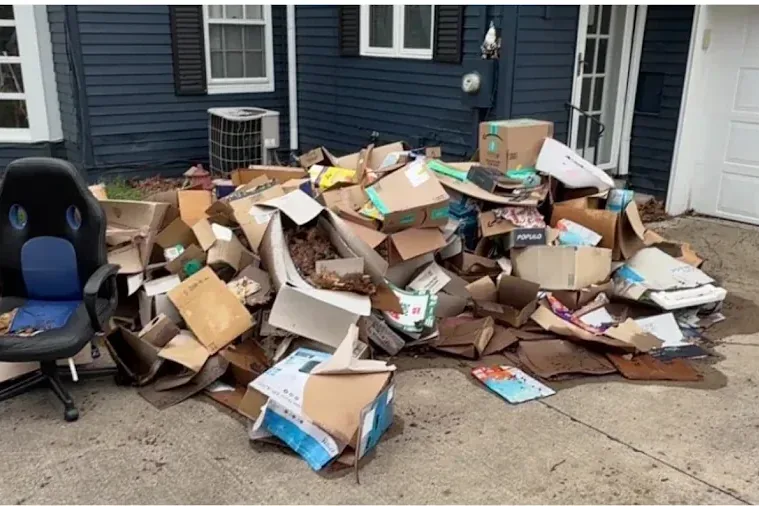 A driveway buried under flattened cardboard moving boxes and a broken office chair.